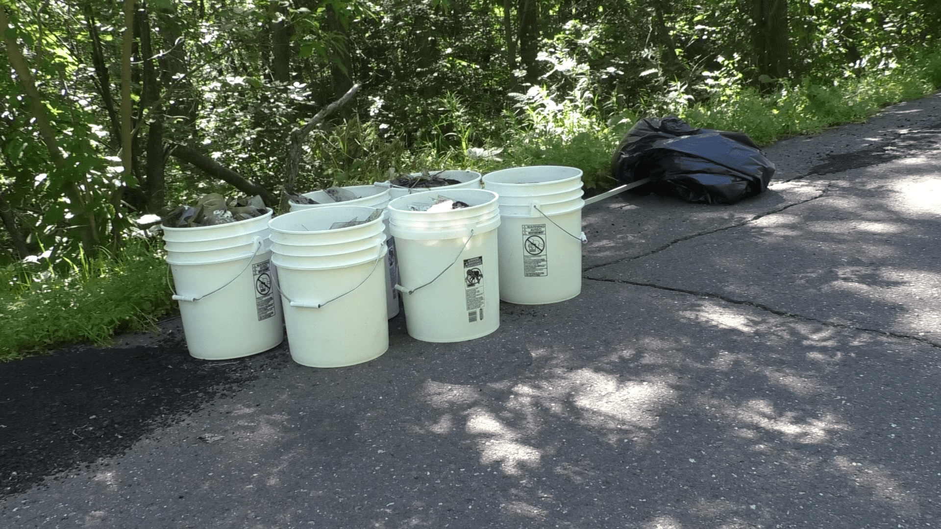Buckets and a black trash bag that is filled with trash that was picked up from the woods