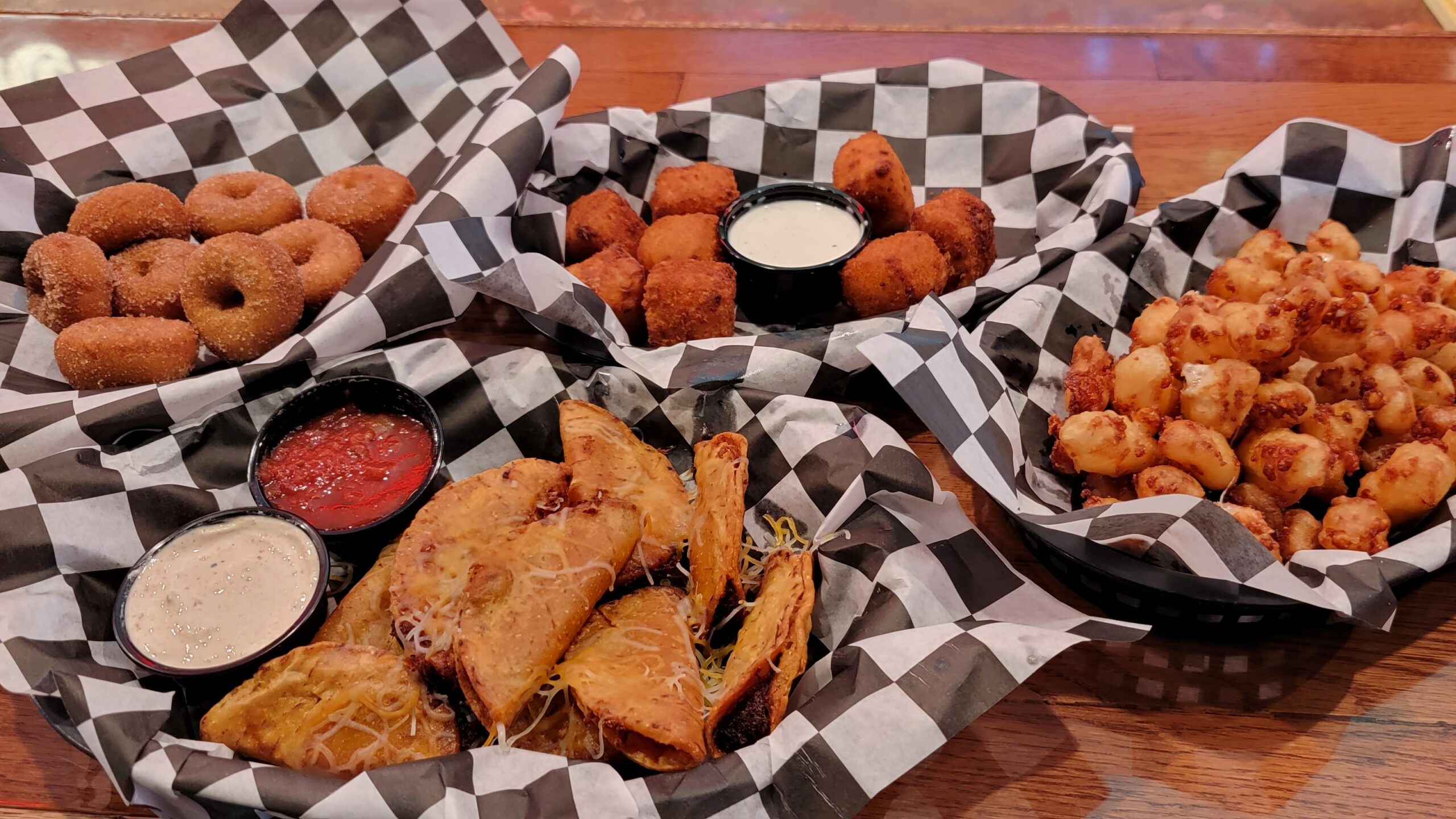 cheese curds, mini donuts, mini tacos, mac-n-cheese bites in baskets with black & white checkered paper