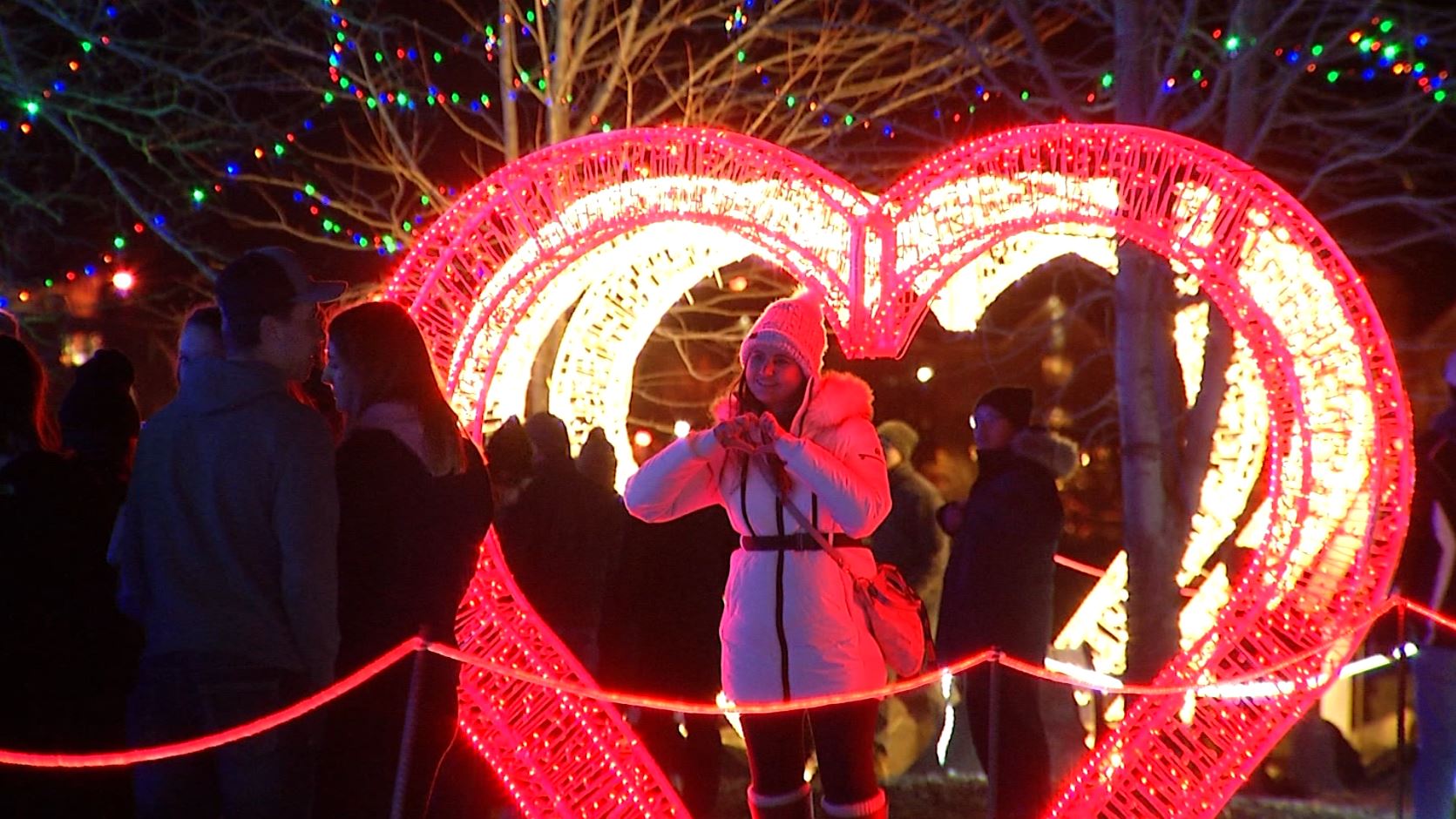 A girl poses in front of a Bentleyville heart light display