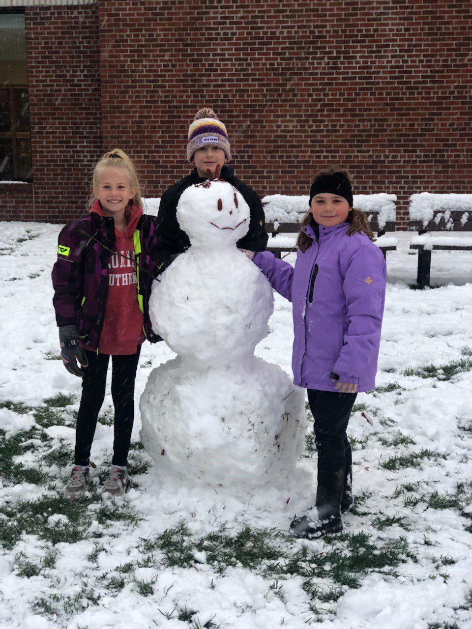 three children stand next to snowman