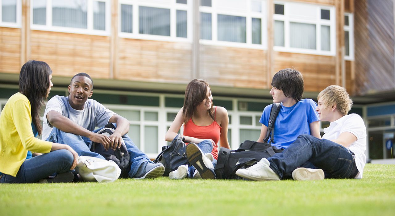 five young adults sit on grass in front of building