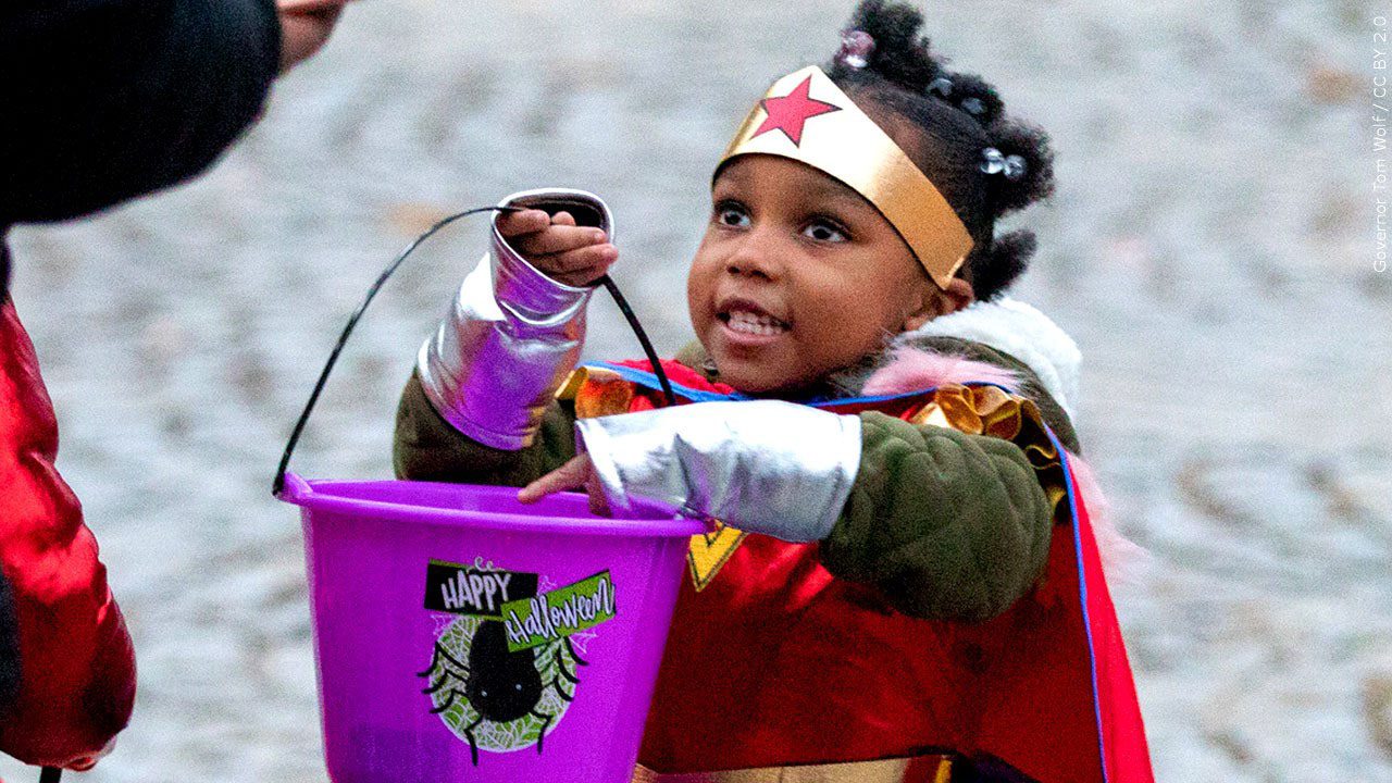 young girl dressed as Wonder Woman with a purple Halloween bucket