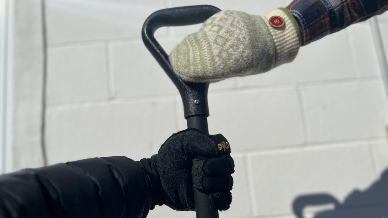 a shovel handle being held by a gloved hand and a mitten