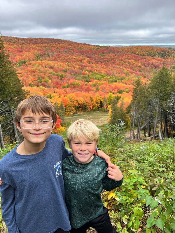 Two boys stand with brilliant fall colors across the hill behind