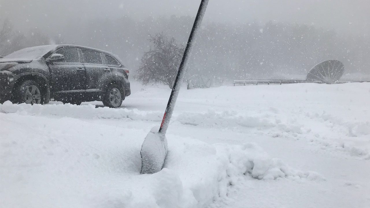 Snowy scene of car in WDIO parking lot and a shovel