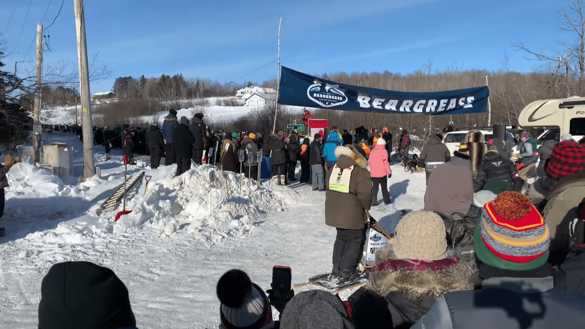giant Beargrease banner marks the starting line with hundreds of people waiting for the mushers.