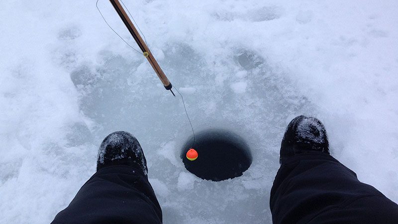 A ice fishing hole with a tip-up and two feet to the sides.