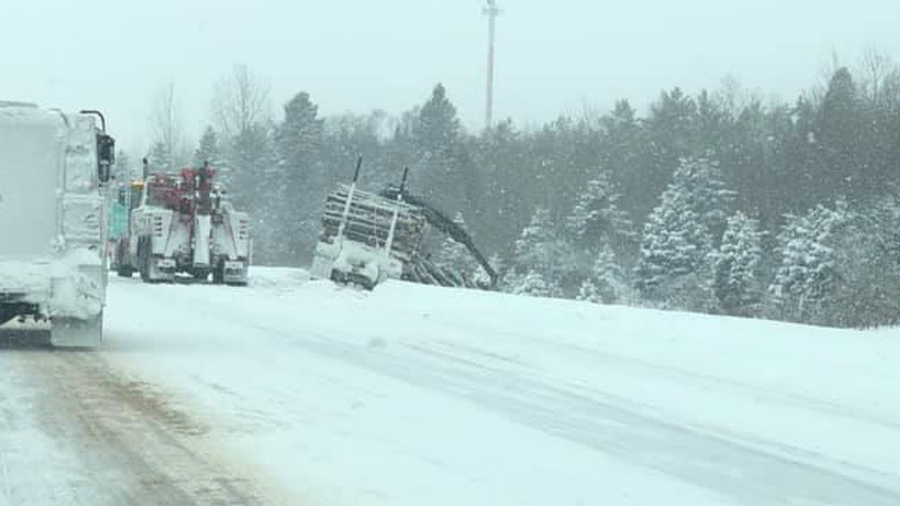 A logging truck has slid into a ditch on a snow roadway.