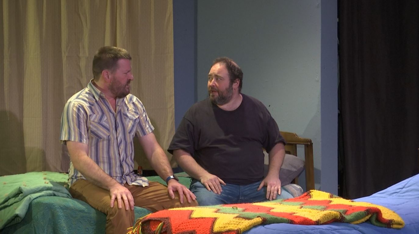 Two "The Boys Room" actors sit on a bed