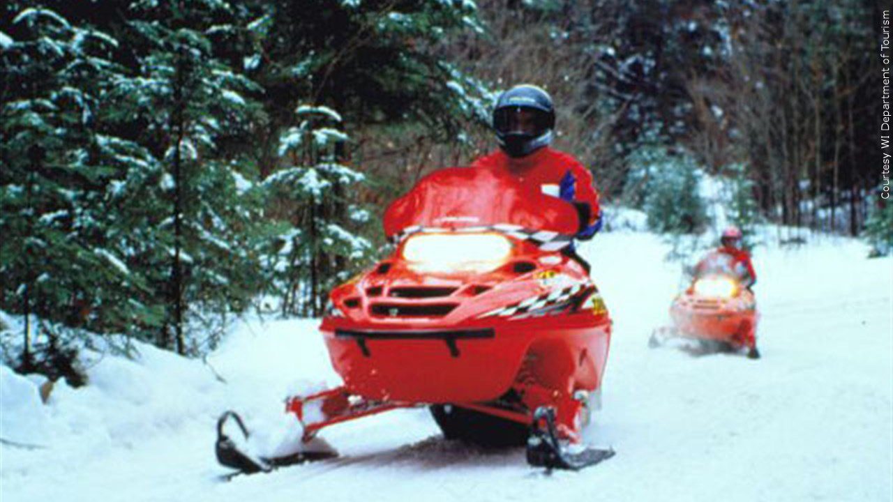 Two red snowmobiles riding on a snow covered trail.