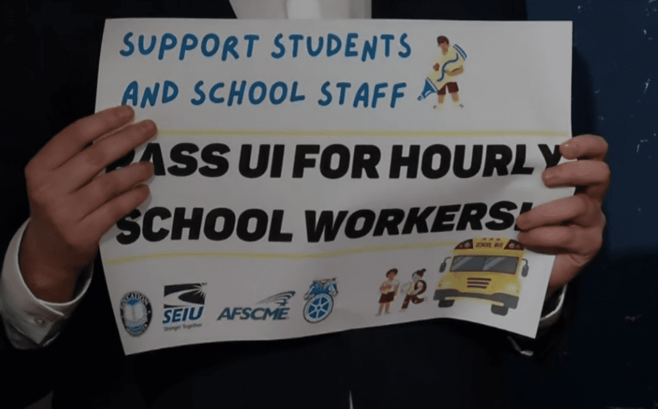 An individual holding a sign stating, "support students and staff pass UI for hourly school workers."