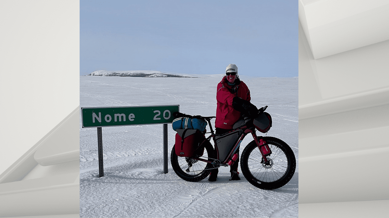 Leah Gruhn and her bike next to a sign for Nome
