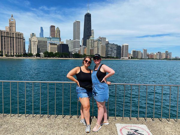 Two sisters stand next to a metal railing with Chicago skyline and water behind them.