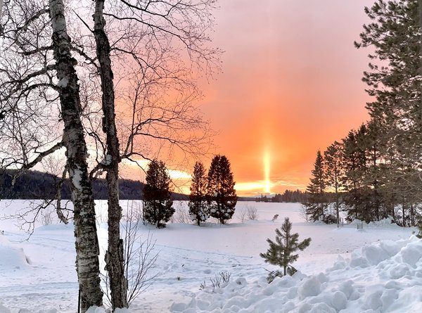 A pillar of bright gold straight up from the setting sun over snowy landscape.