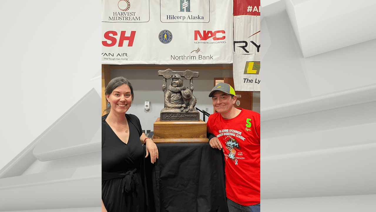 Sarah Keefer and Ryan Redington stand next to the Iditarod trophy