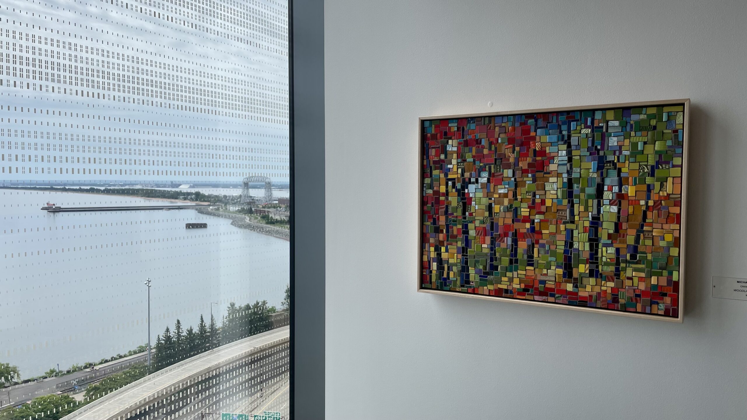 Art fills a corner of a wall near a window with a view of the Lift Bridge.