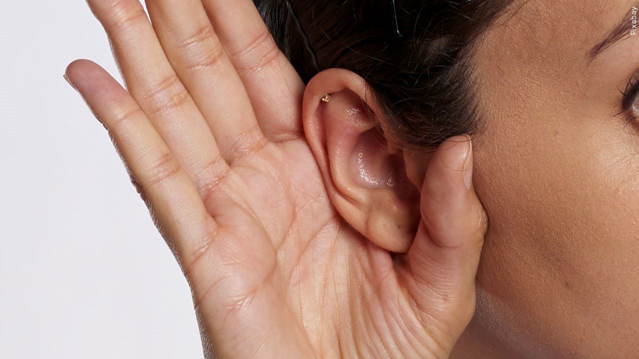 A woman making a listening motion near her ear
