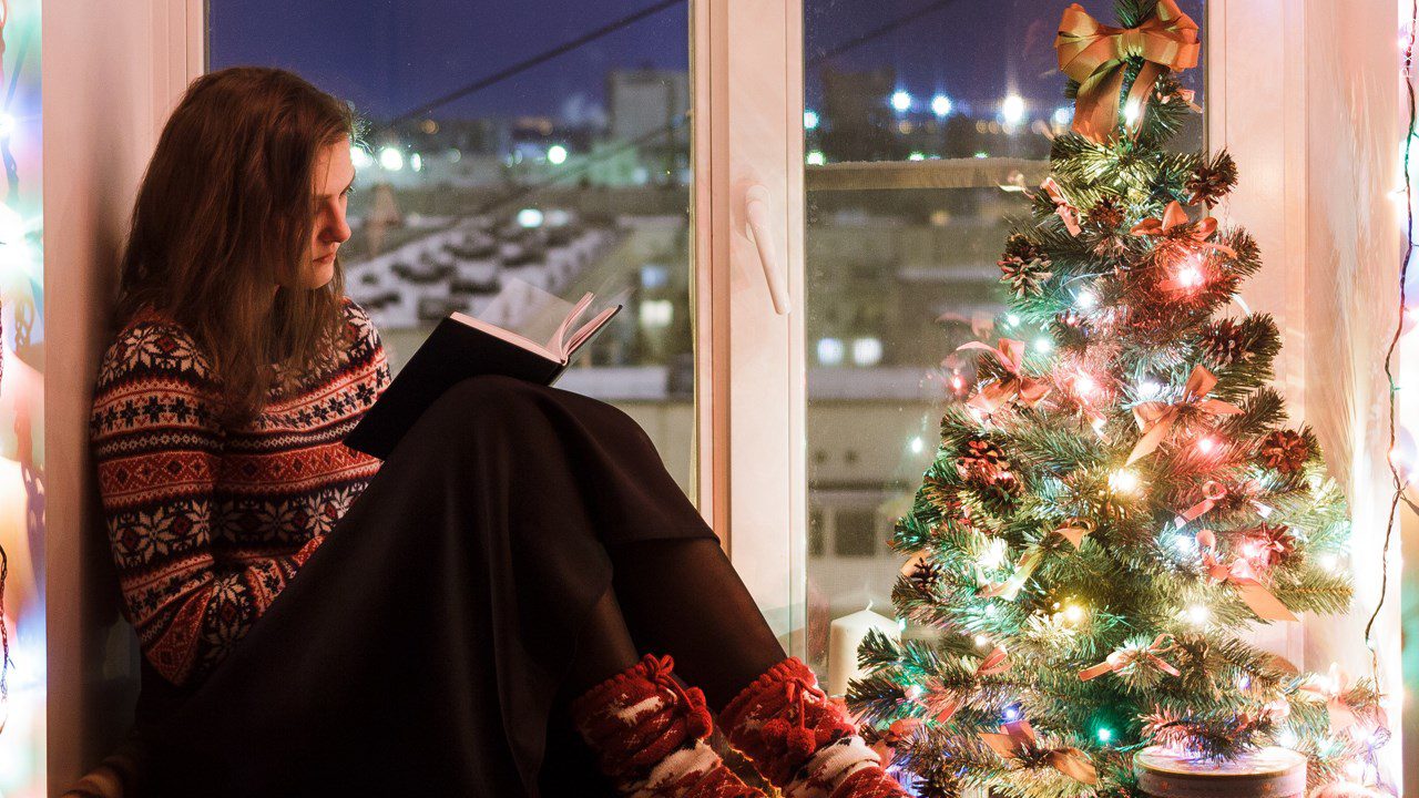 A woman reads by a Christmas tree
