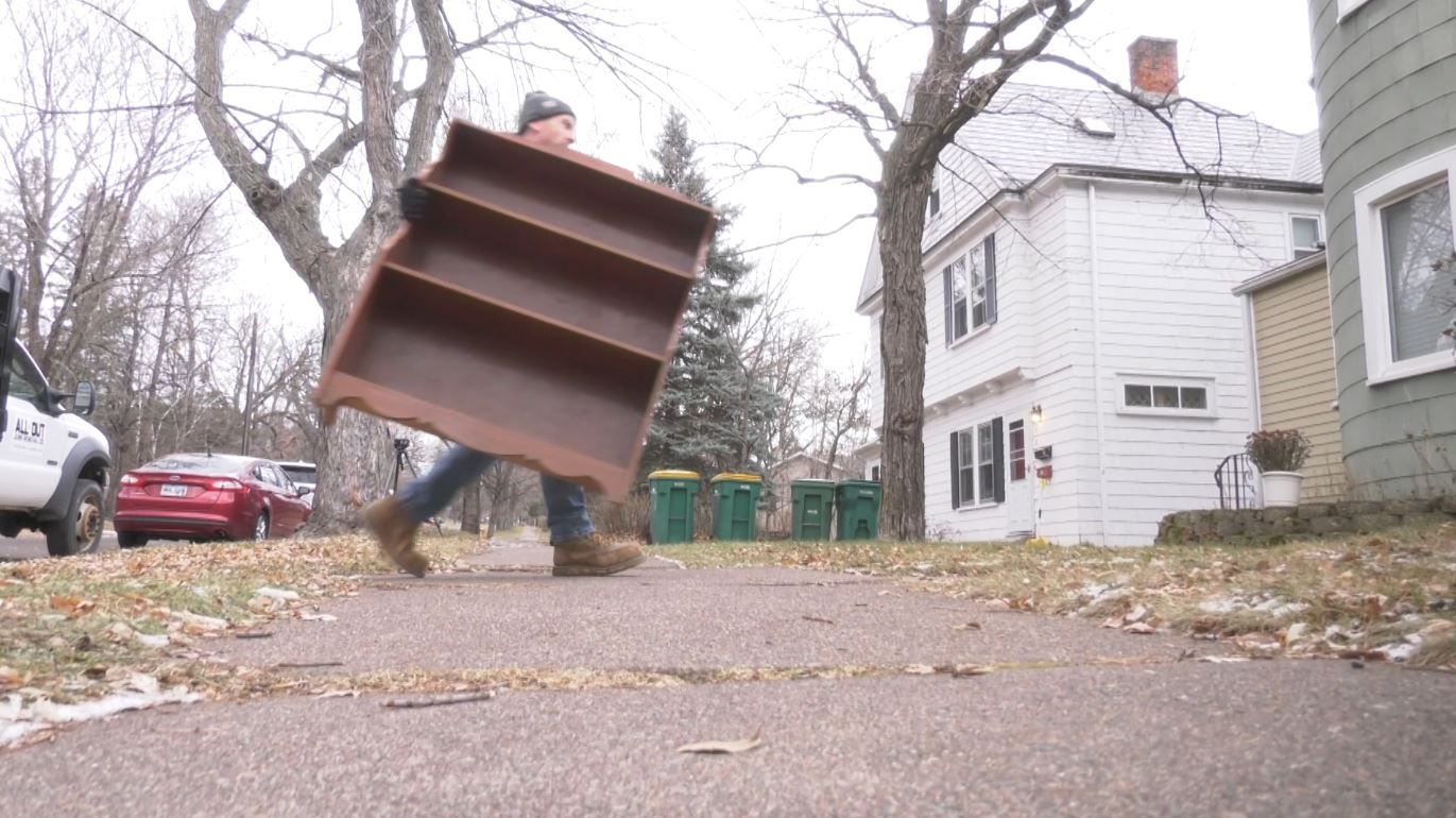 Charlie Martin carries a bookshelf up to a house