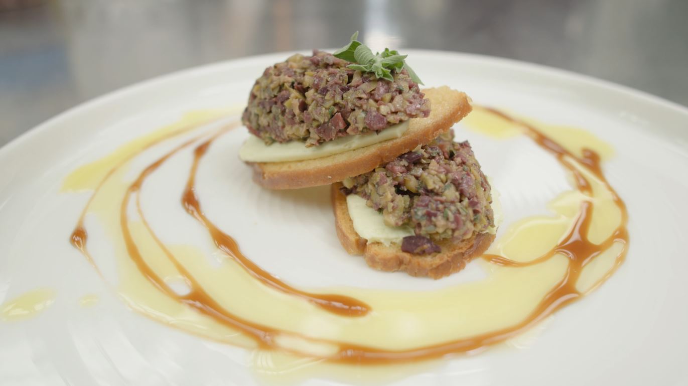 A crostini topped with basil chevre and olive tapenade
